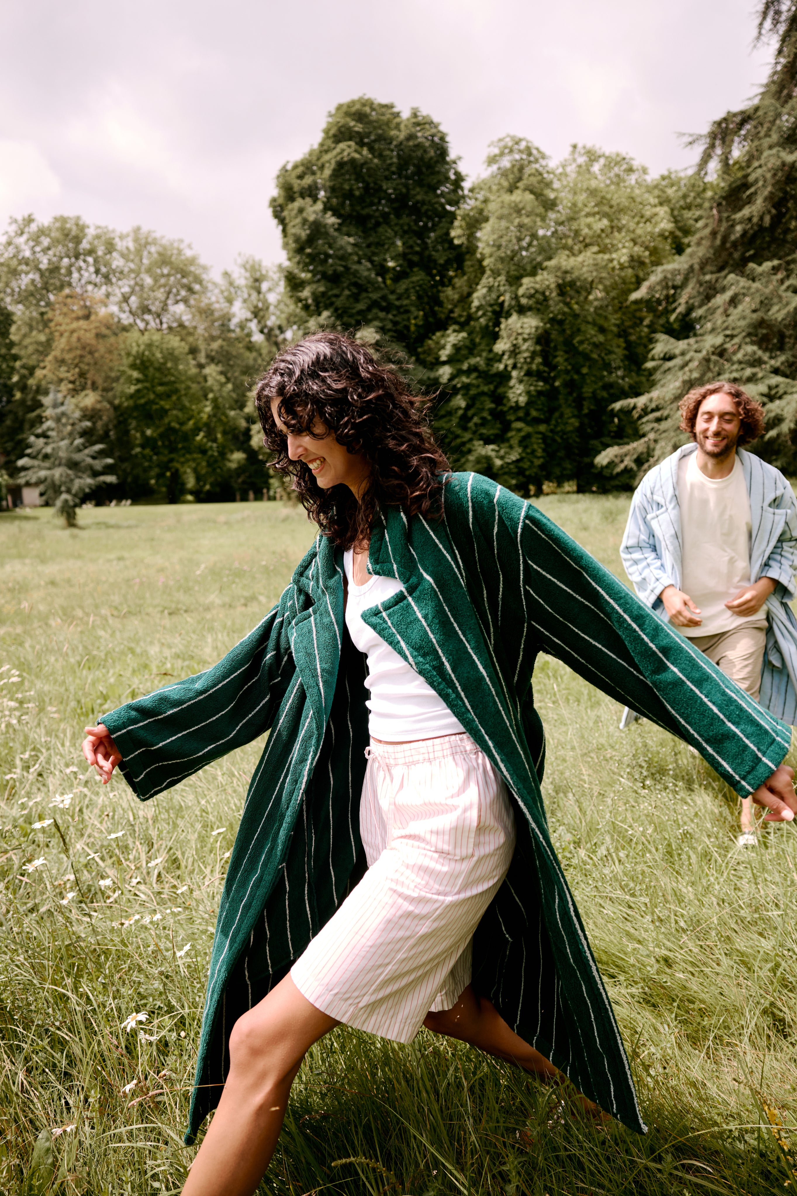 Woman in a Hommey Robe running through a grassy field with a man in the background.